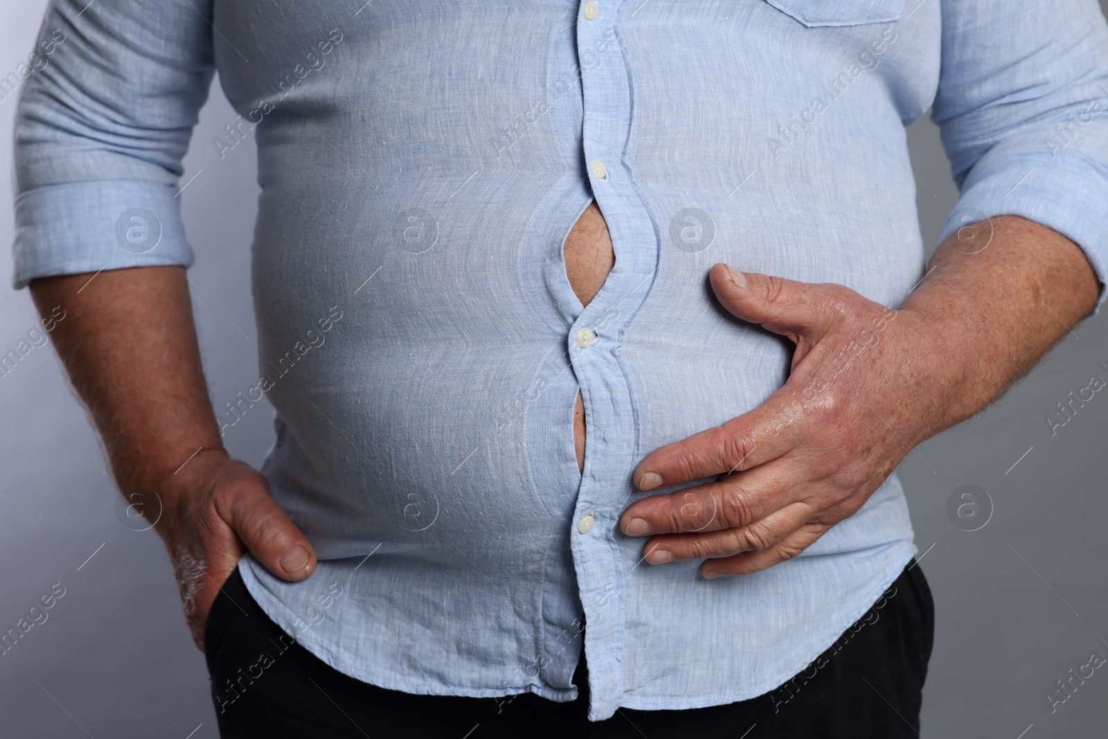 Photo of Overweight man in tight shirt on grey background, closeup