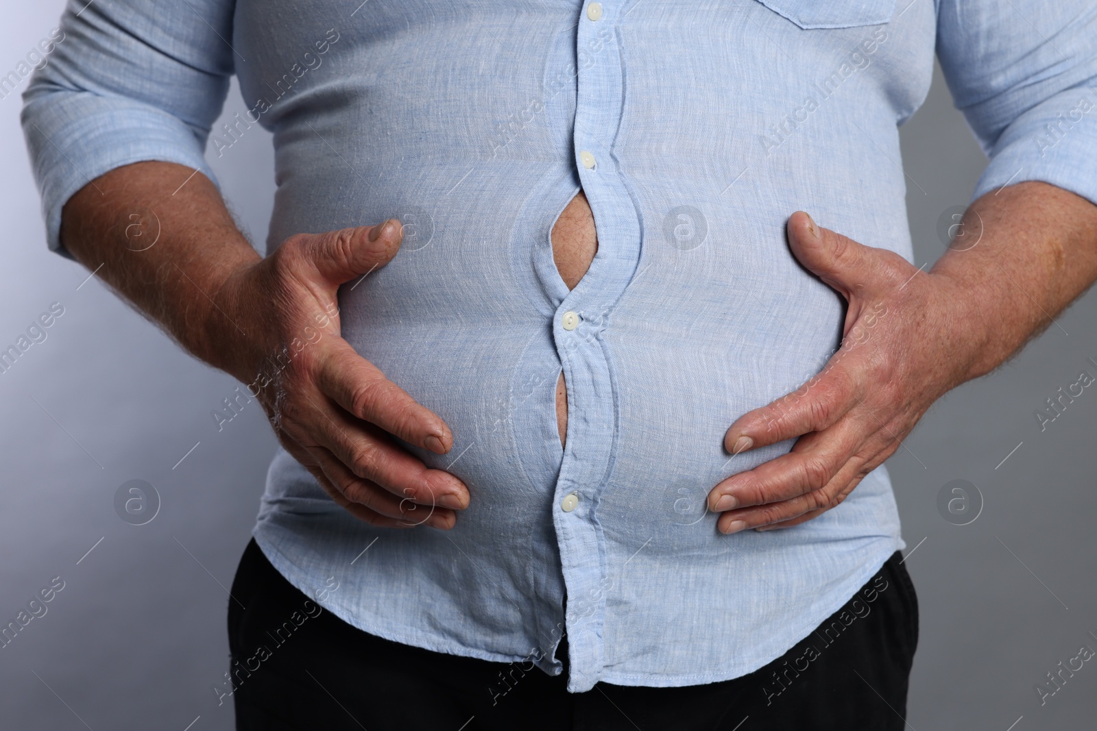 Photo of Overweight man in tight shirt on grey background, closeup