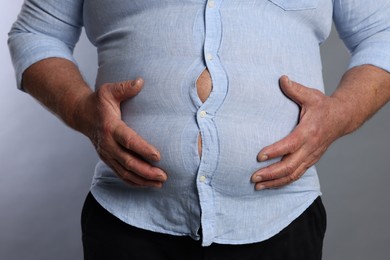 Photo of Overweight man in tight shirt on grey background, closeup