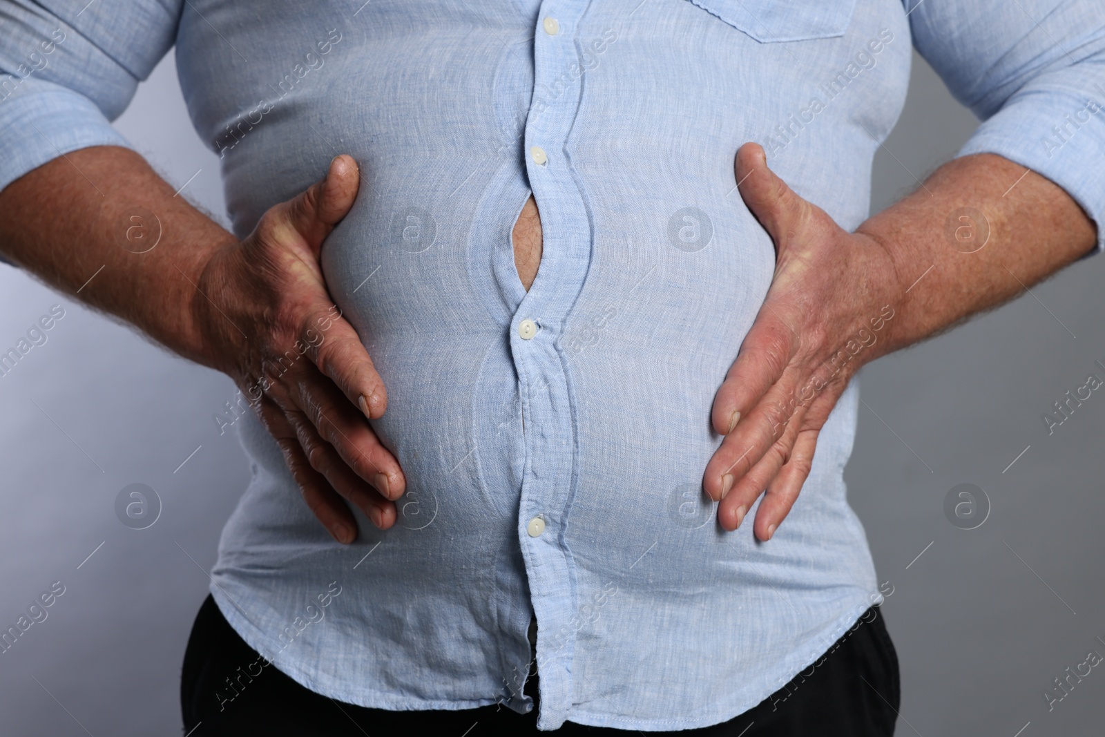 Photo of Overweight man in tight shirt on grey background, closeup