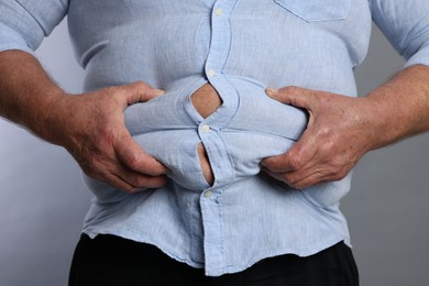 Photo of Overweight man in tight shirt on grey background, closeup