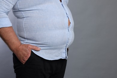 Photo of Overweight man in tight shirt on grey background, closeup. Space for text