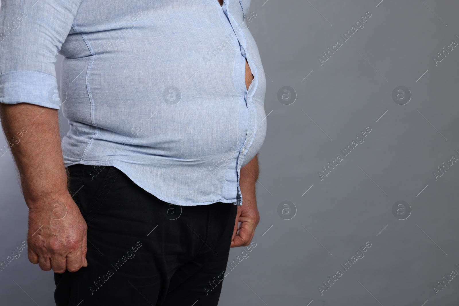 Photo of Overweight man in tight shirt on grey background, closeup. Space for text