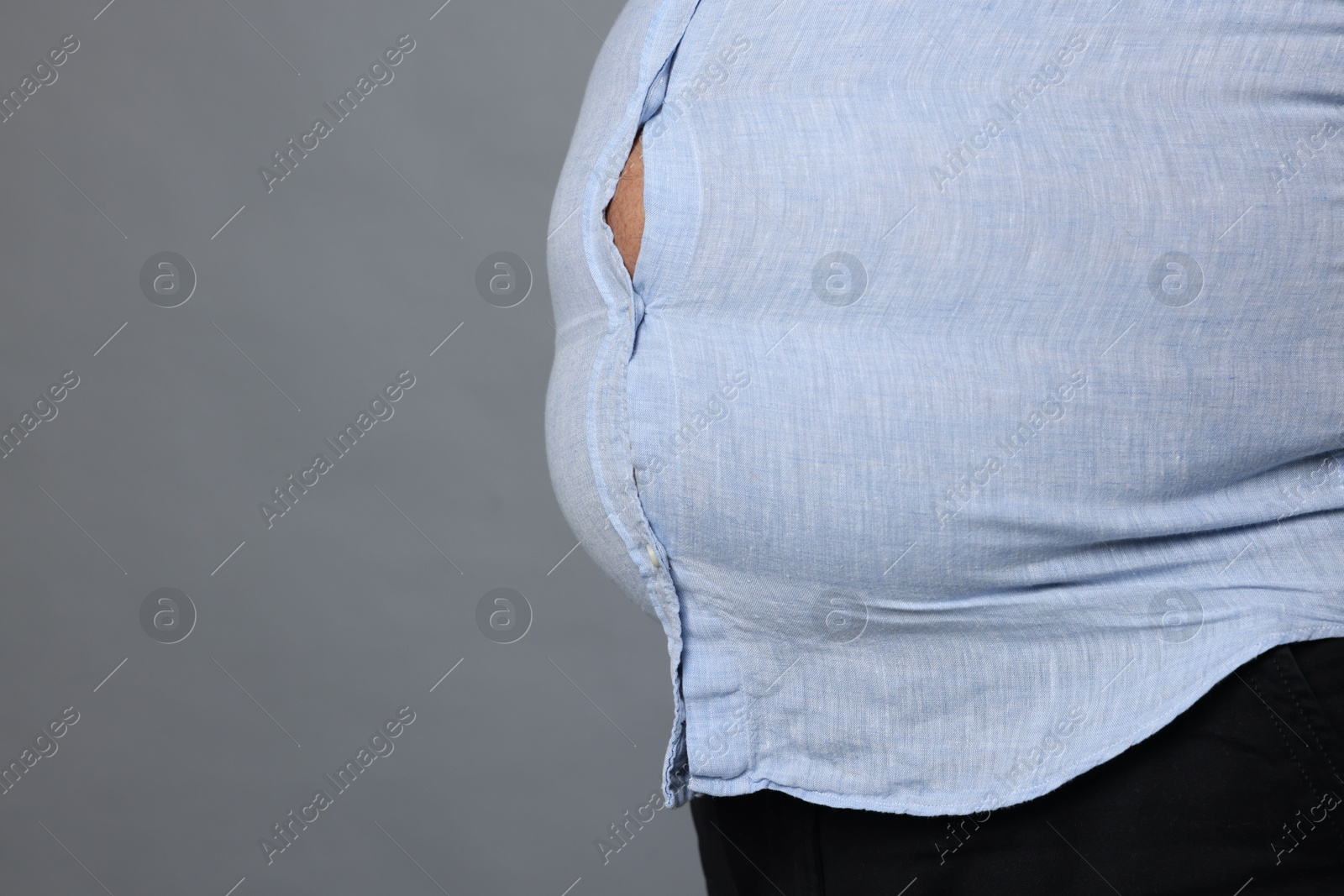 Photo of Overweight man in tight shirt on grey background, closeup. Space for text