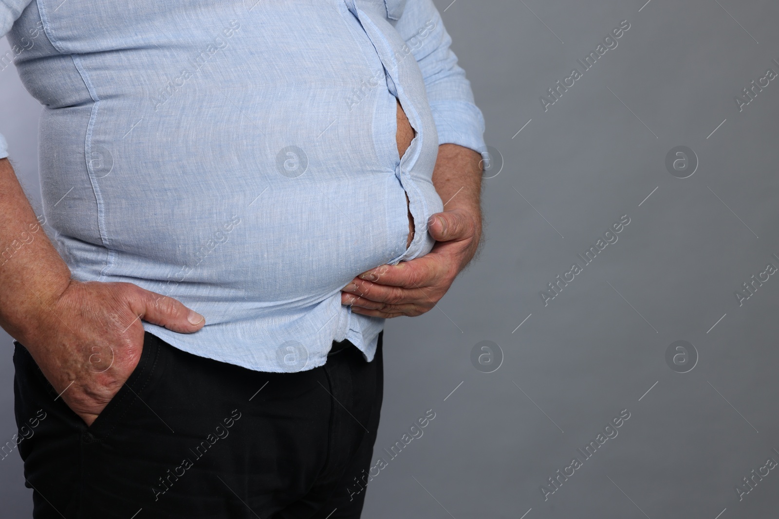 Photo of Overweight man in tight shirt on grey background, closeup. Space for text