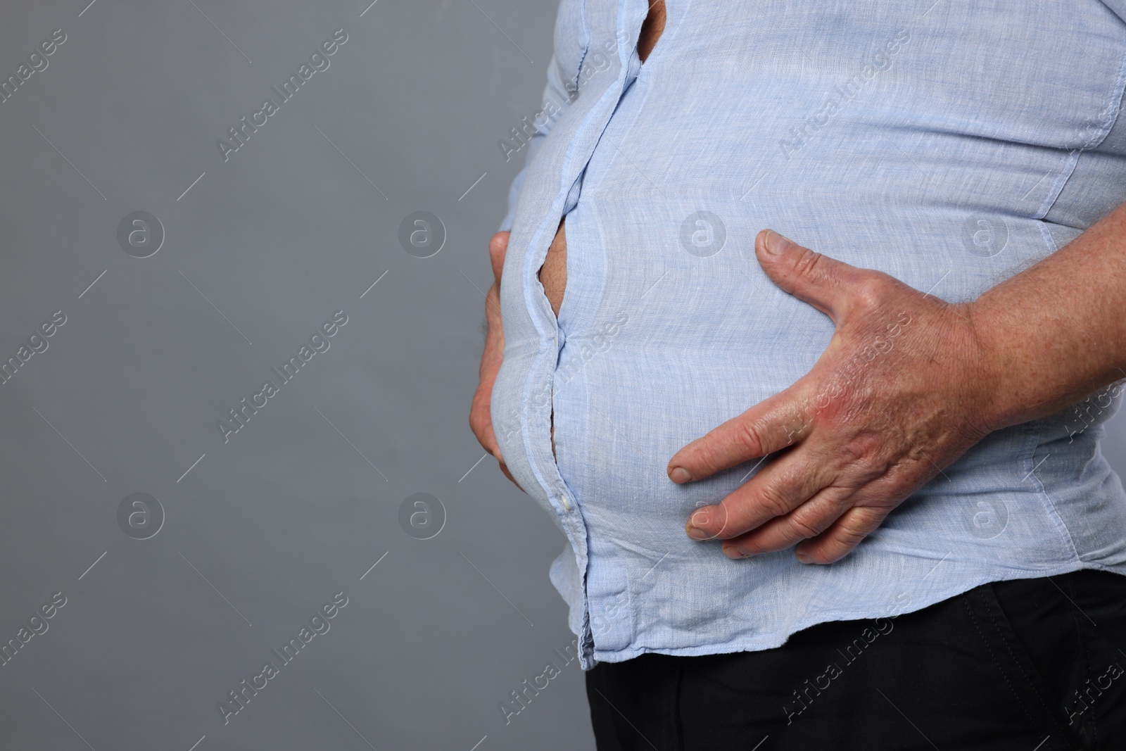 Photo of Overweight man in tight shirt on grey background, closeup. Space for text