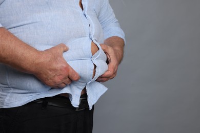 Photo of Overweight man in tight shirt on grey background, closeup. Space for text