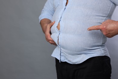 Photo of Overweight man in tight shirt on grey background, closeup. Space for text