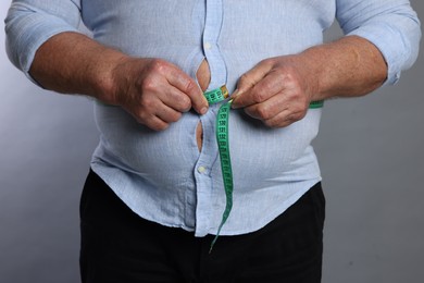 Photo of Overweight man measuring his belly with tape on grey background, closeup