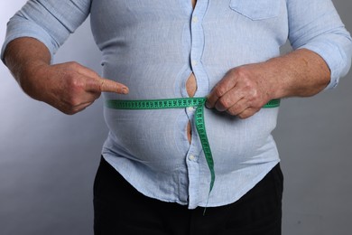 Photo of Overweight man measuring his belly with tape on grey background, closeup