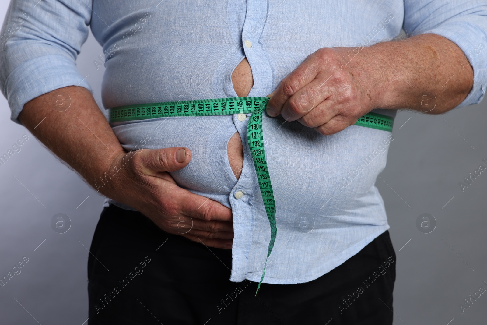 Photo of Overweight man measuring his belly with tape on grey background, closeup