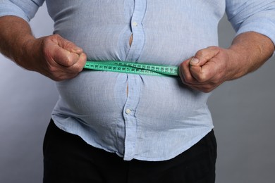 Photo of Overweight man measuring his belly with tape on grey background, closeup