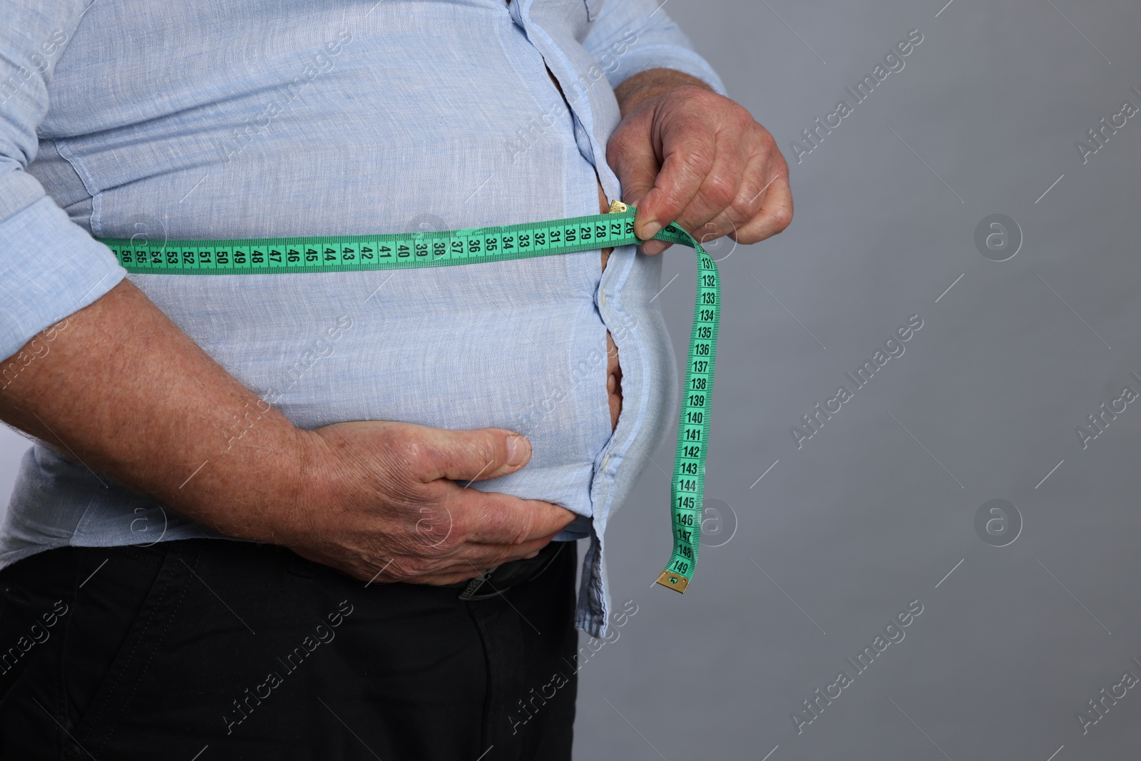 Photo of Overweight man measuring his belly with tape on grey background, closeup. Space for text