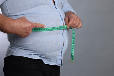 Photo of Overweight man measuring his belly with tape on grey background, closeup. Space for text