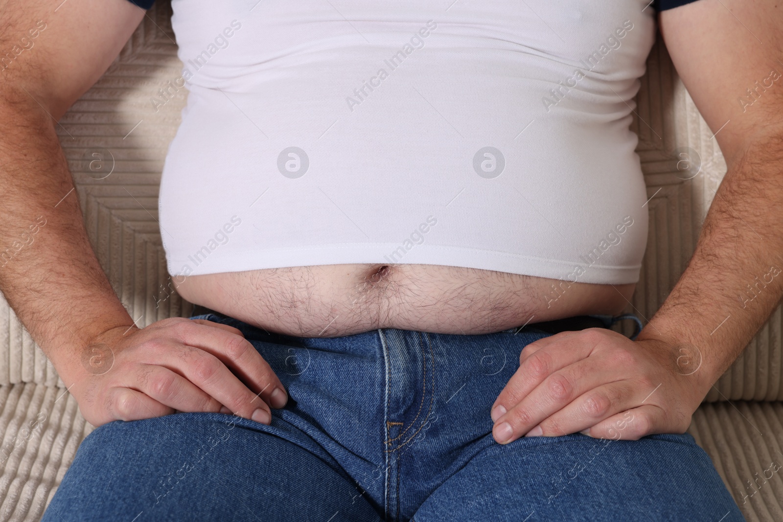 Photo of Overweight man in tight t-shirt on sofa indoors, closeup