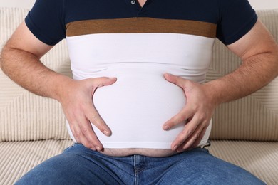 Photo of Overweight man in tight t-shirt on sofa indoors, closeup