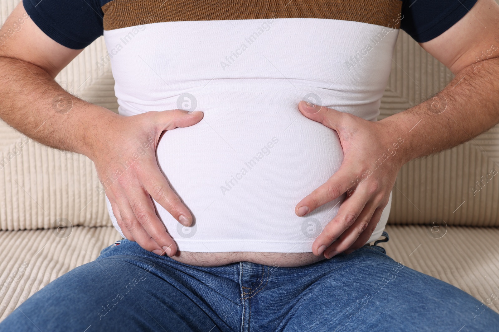 Photo of Overweight man in tight t-shirt on sofa indoors, closeup