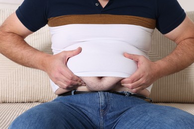 Photo of Overweight man in tight t-shirt on sofa indoors, closeup