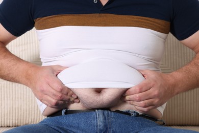 Photo of Overweight man in tight t-shirt on sofa indoors, closeup