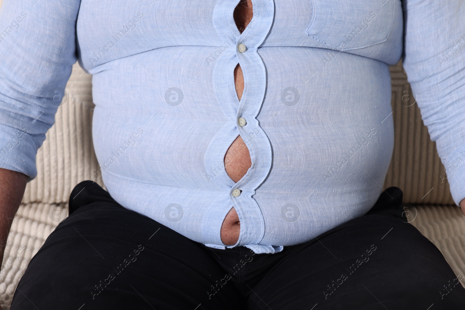 Photo of Overweight man in tight shirt on sofa indoors, closeup