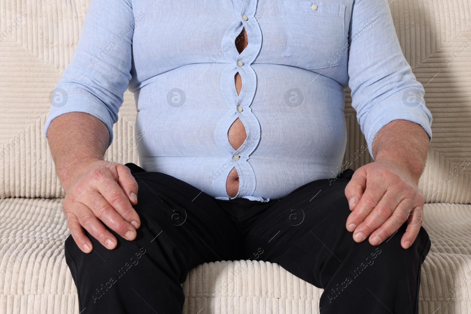 Photo of Overweight man in tight shirt on sofa indoors, closeup