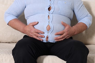 Photo of Overweight man in tight shirt on sofa indoors, closeup