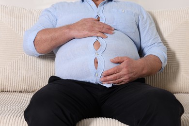 Photo of Overweight man in tight shirt on sofa indoors, closeup