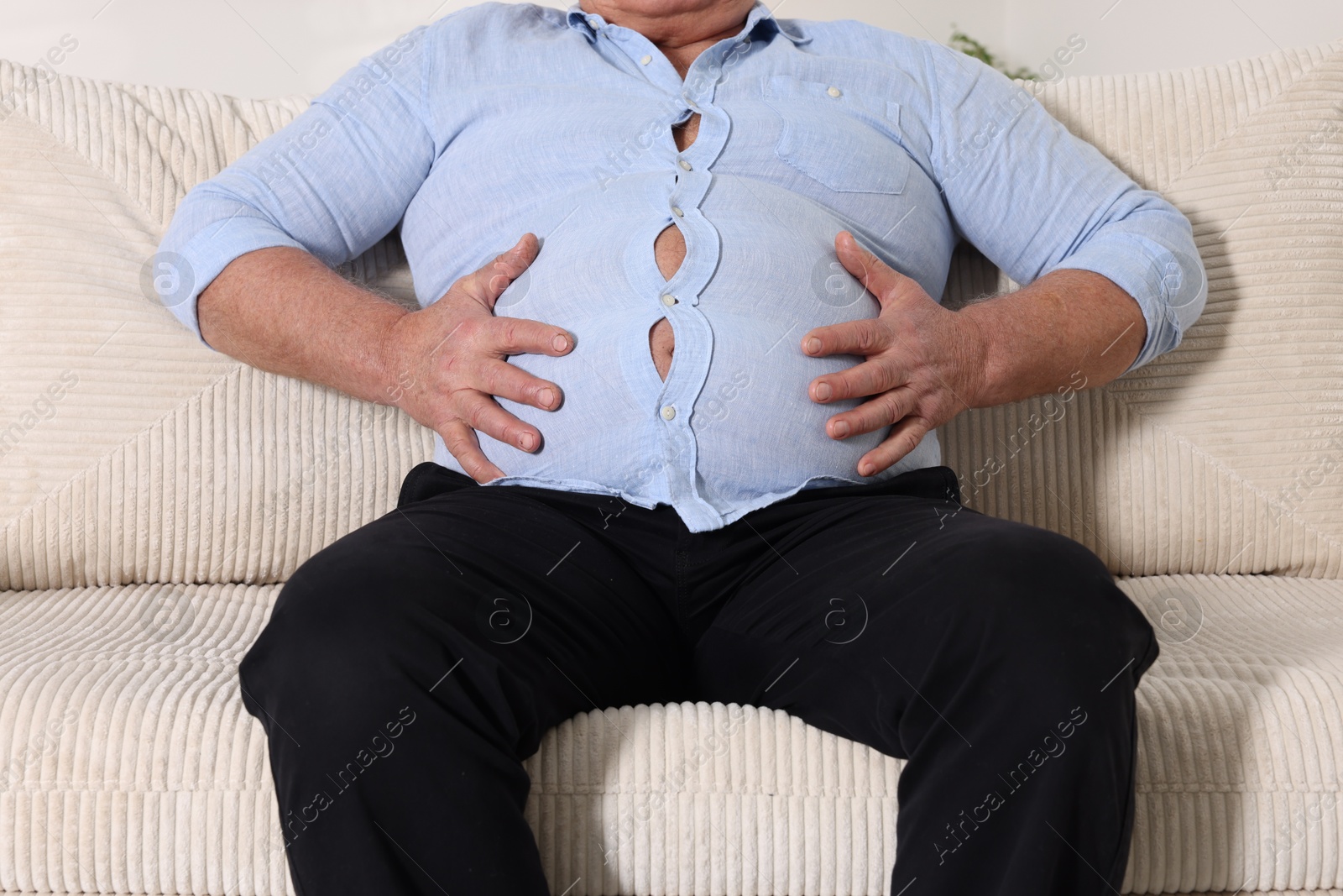 Photo of Overweight man in tight shirt on sofa indoors, closeup