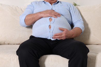 Photo of Overweight man in tight shirt on sofa indoors, closeup