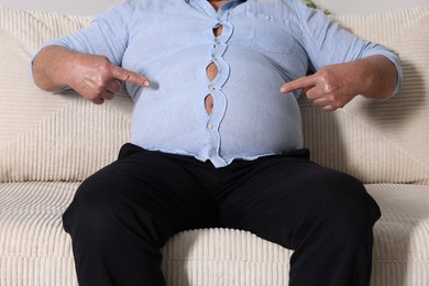 Photo of Overweight man in tight shirt on sofa indoors, closeup