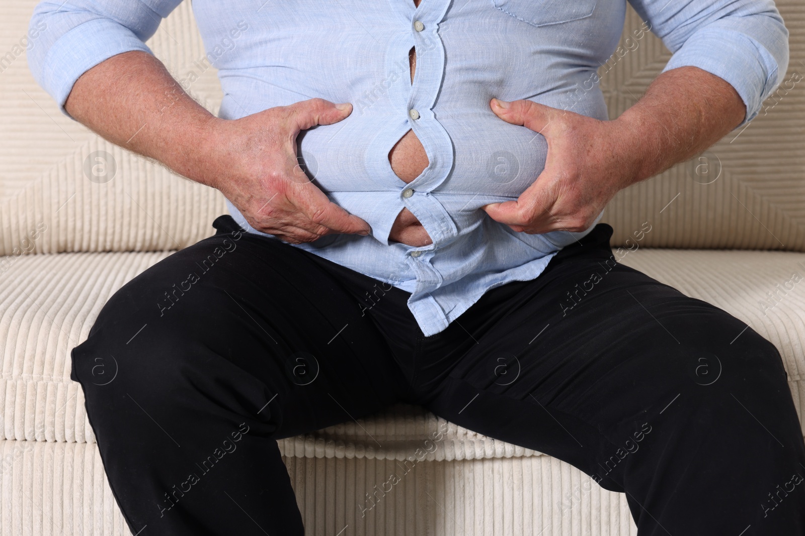 Photo of Overweight man in tight shirt on sofa indoors, closeup