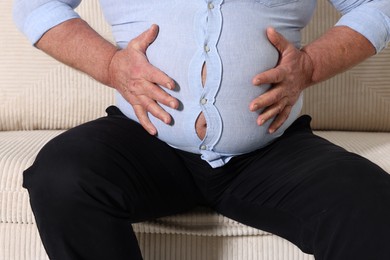 Photo of Overweight man in tight shirt on sofa indoors, closeup