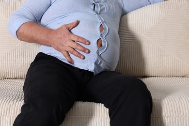 Photo of Overweight man in tight shirt on sofa indoors, closeup