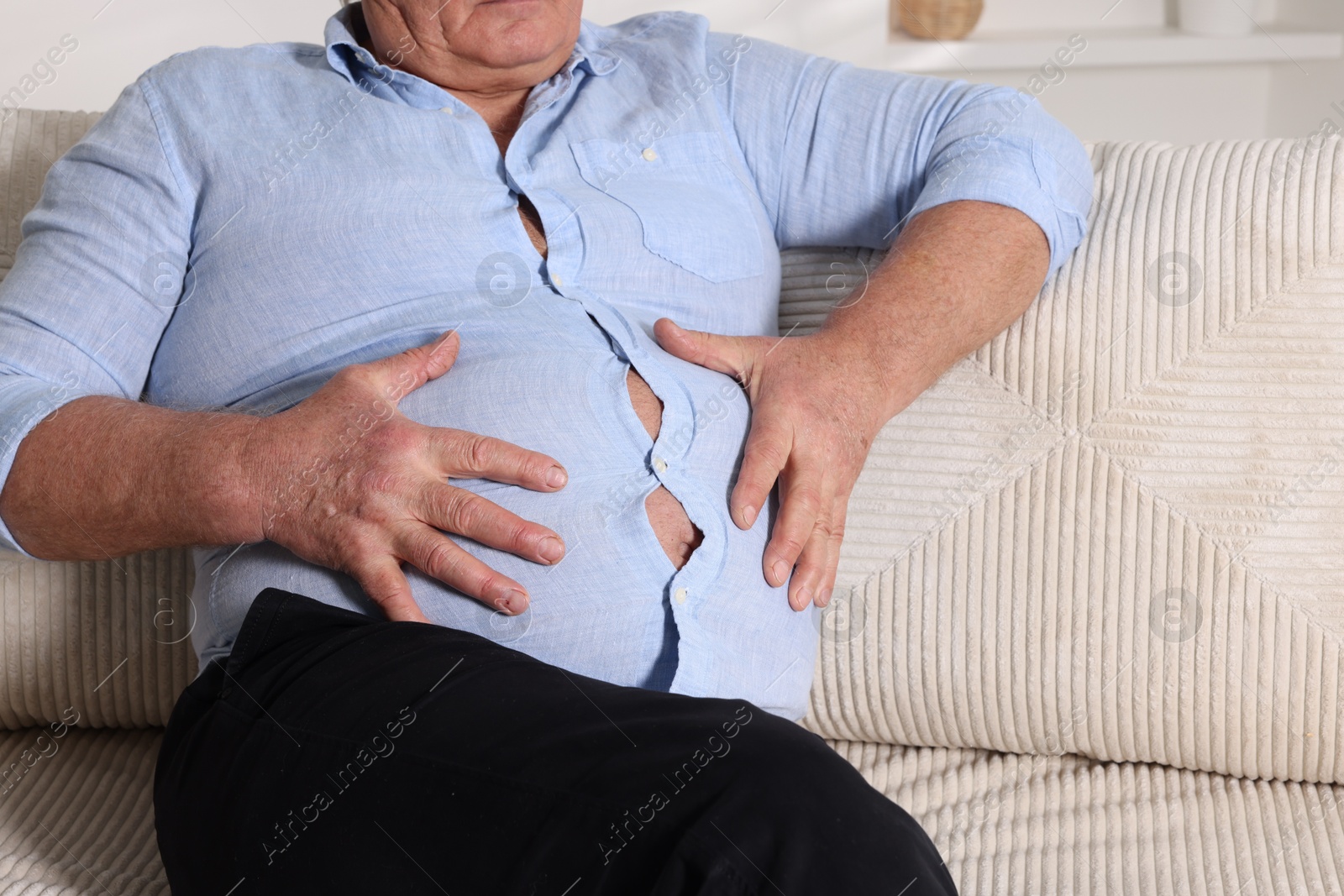 Photo of Overweight man in tight shirt on sofa indoors, closeup