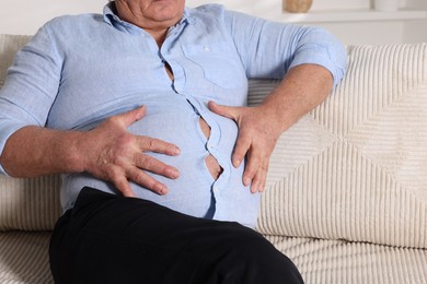 Photo of Overweight man in tight shirt on sofa indoors, closeup