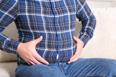 Photo of Overweight man in tight shirt on sofa indoors, closeup