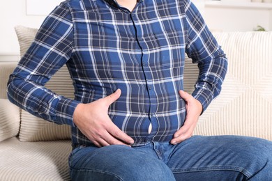 Photo of Overweight man in tight shirt on sofa indoors, closeup