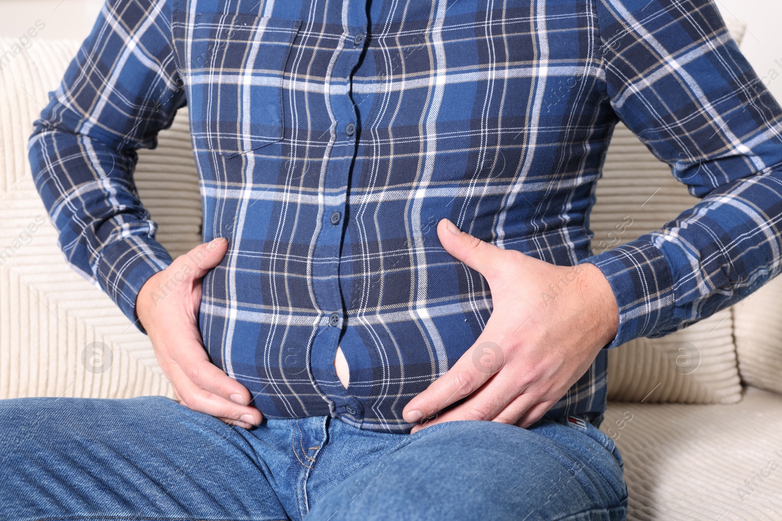 Photo of Overweight man in tight shirt on sofa indoors, closeup