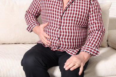 Photo of Overweight man in tight shirt on sofa indoors, closeup