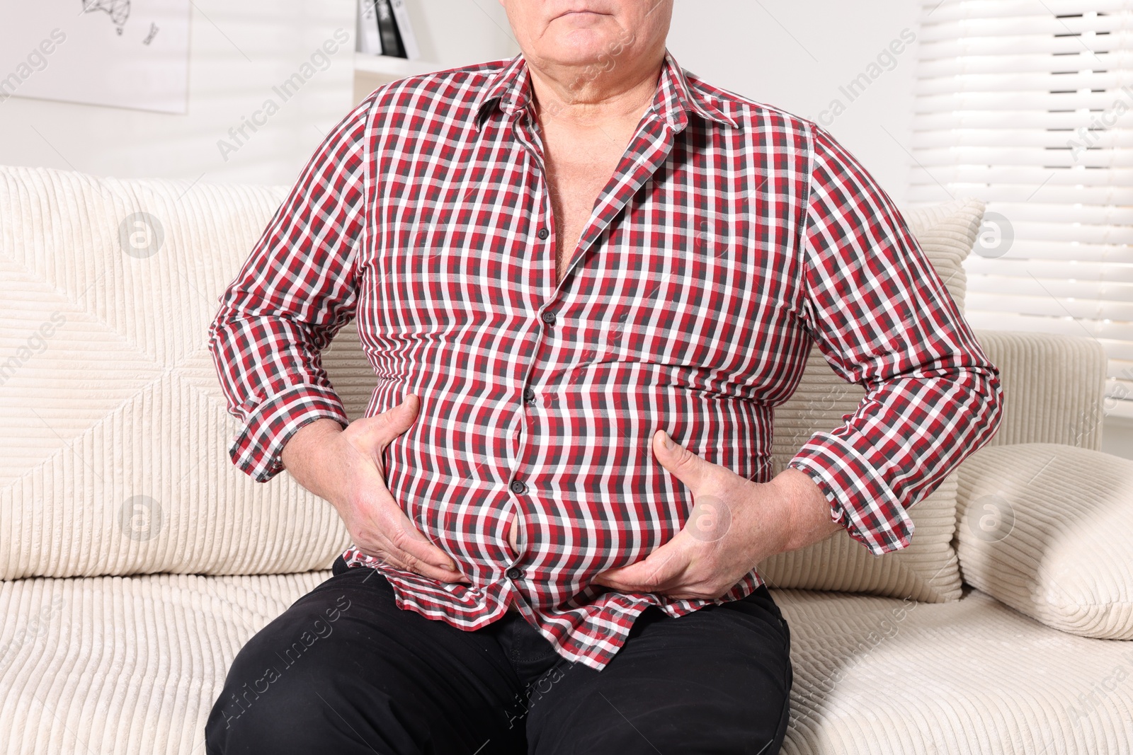 Photo of Overweight man in tight shirt on sofa indoors, closeup