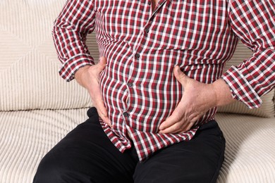 Photo of Overweight man in tight shirt on sofa indoors, closeup