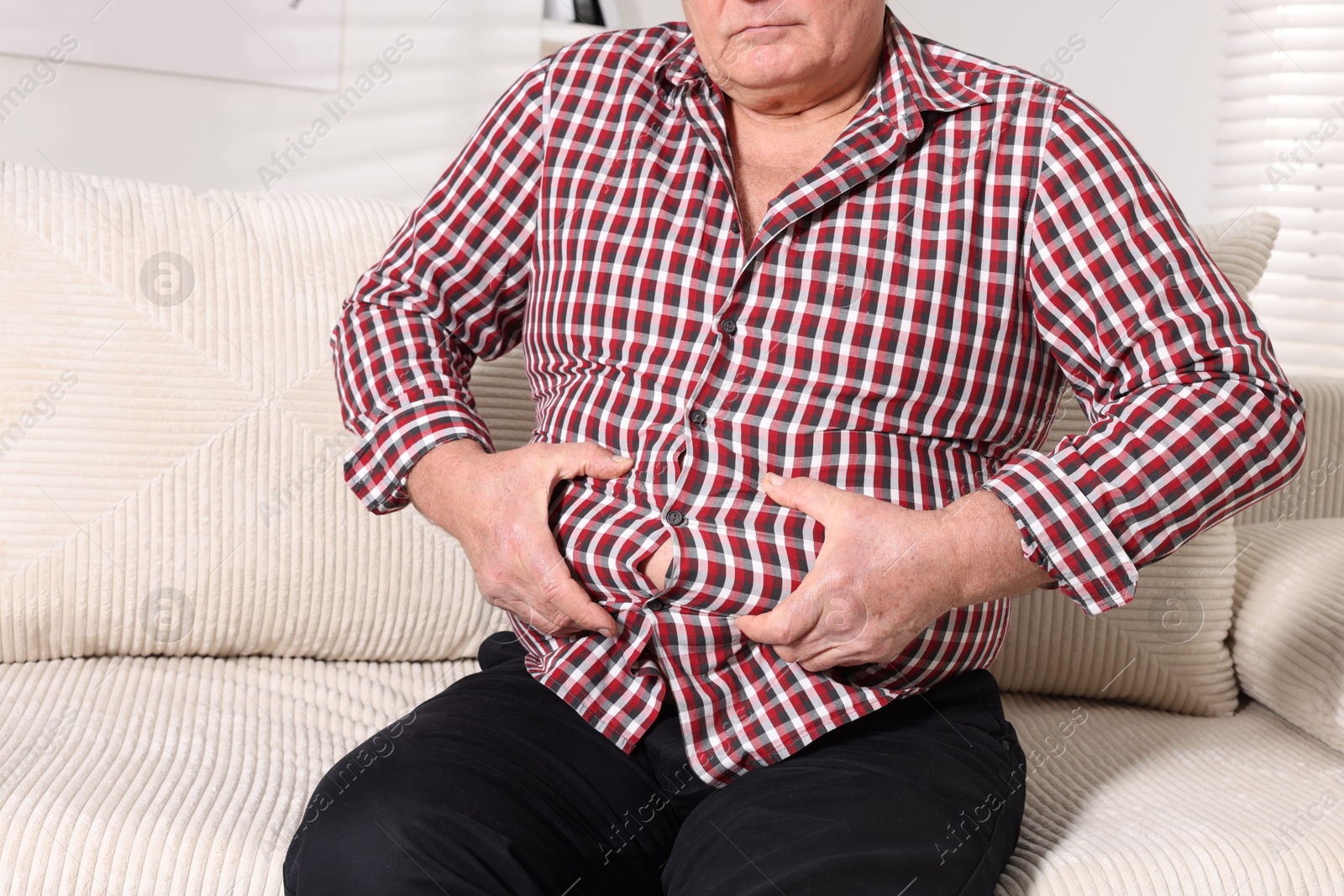 Photo of Overweight man in tight shirt on sofa indoors, closeup