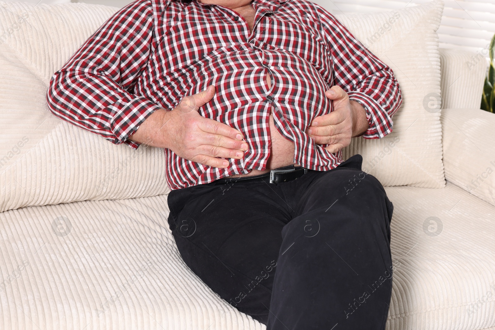 Photo of Overweight man in tight shirt on sofa indoors, closeup