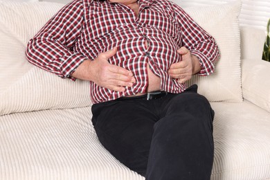 Photo of Overweight man in tight shirt on sofa indoors, closeup