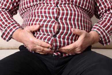 Photo of Overweight man in tight shirt on sofa indoors, closeup