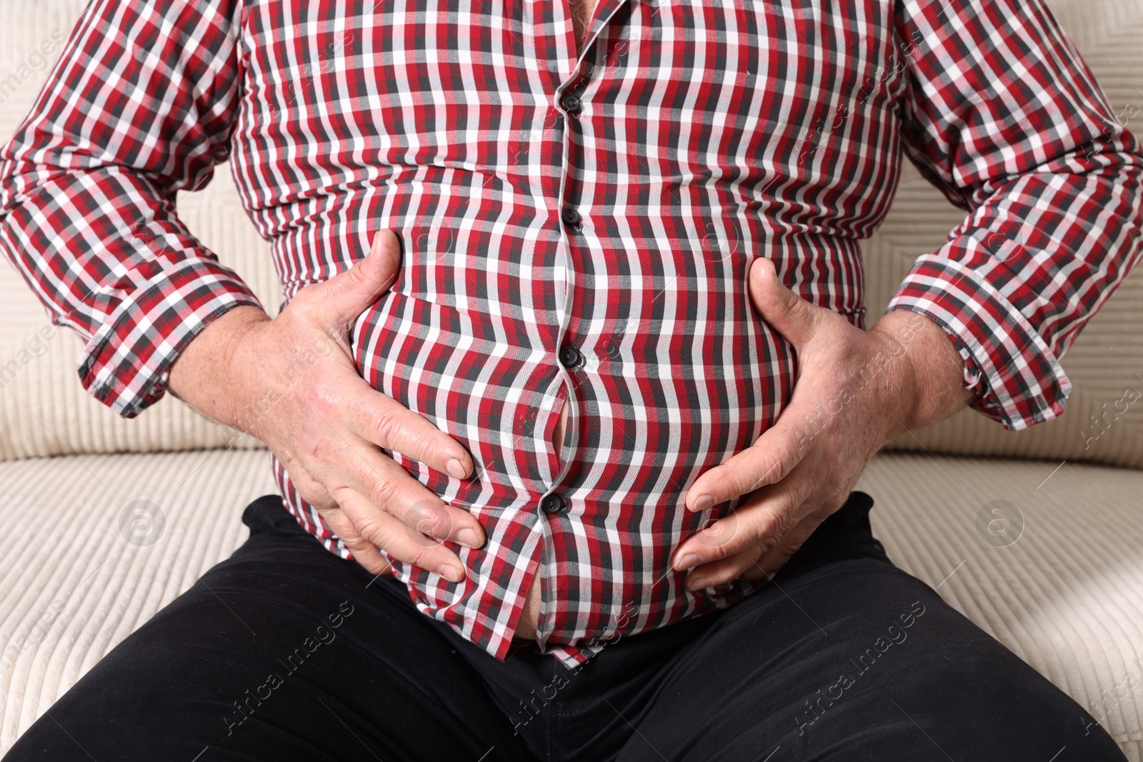 Photo of Overweight man in tight shirt on sofa indoors, closeup