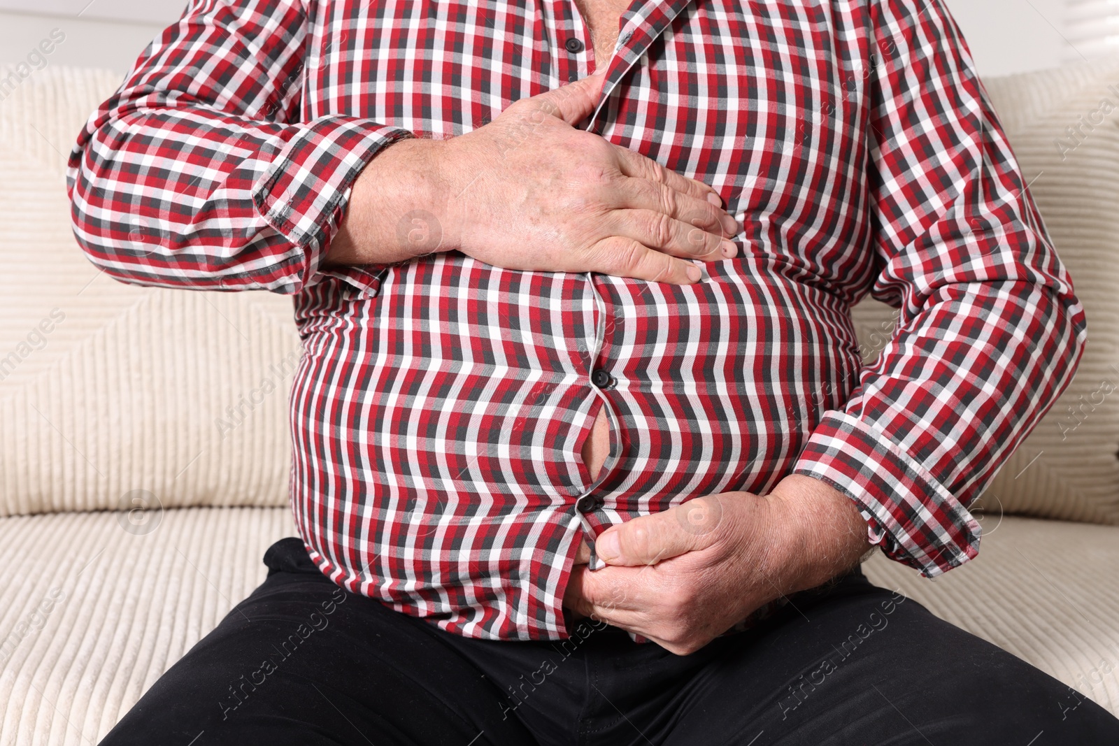 Photo of Overweight man in tight shirt on sofa indoors, closeup