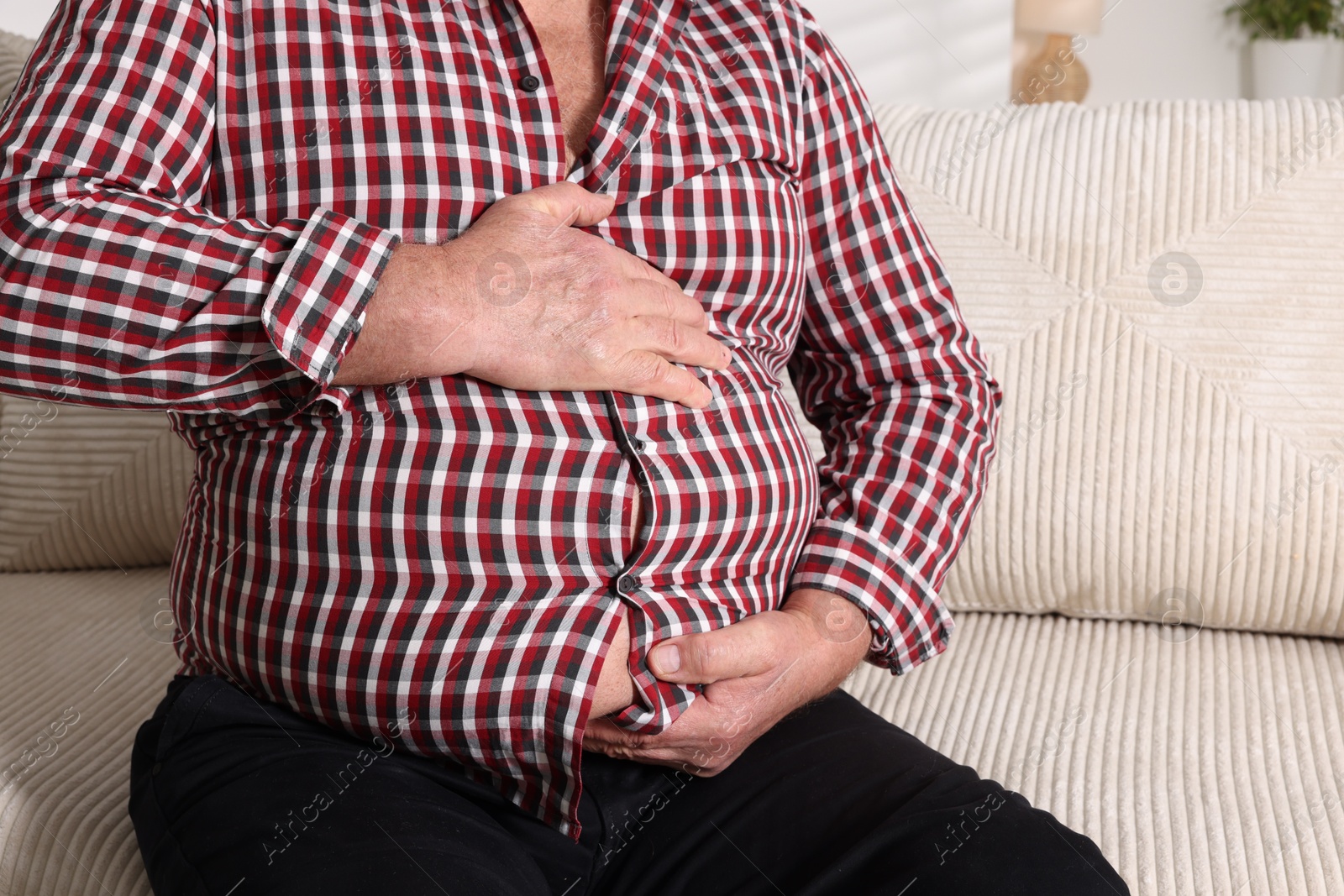 Photo of Overweight man in tight shirt on sofa indoors, closeup