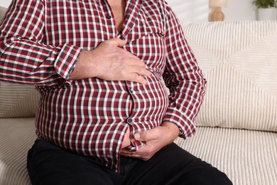 Photo of Overweight man in tight shirt on sofa indoors, closeup