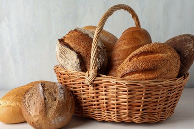 Photo of Different freshly baked bread loafs and wicker basket on white wooden table, closeup